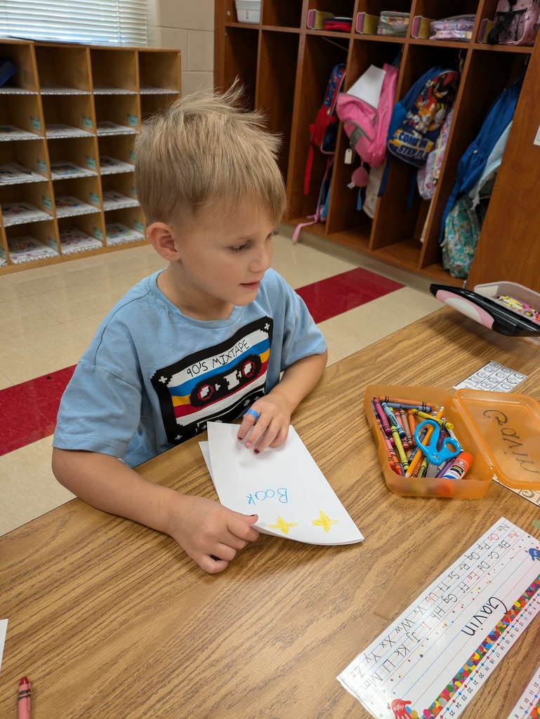 Kindergarten student works at his desk creating a book.