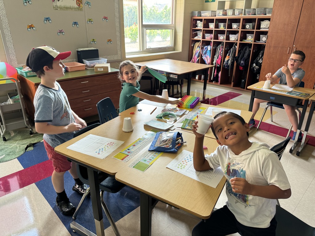 three third grade students are sitting at their desks using styrofoam cups and counters to complete a math activity and worksheet