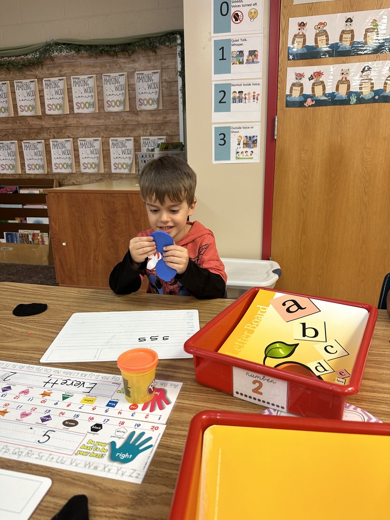 a kindergarten student sits at his desk and practices making the "s" sound while holding a mirror up t o his face