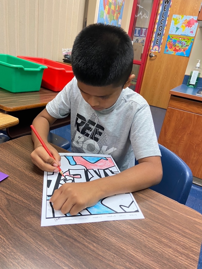 one student sits at his desk and colors a piece of a mural red and blue