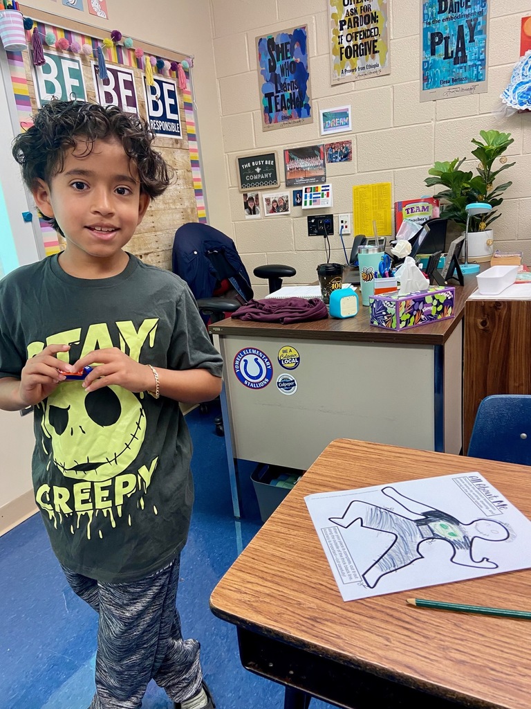 one student stands next to a desk and on the desk there is a coloring sheet that he completed to show things that he likes