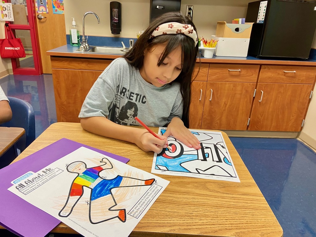 one young lady sits at a desk and colors in a piece of a mural that will be displayed for Hispanic Heritage month