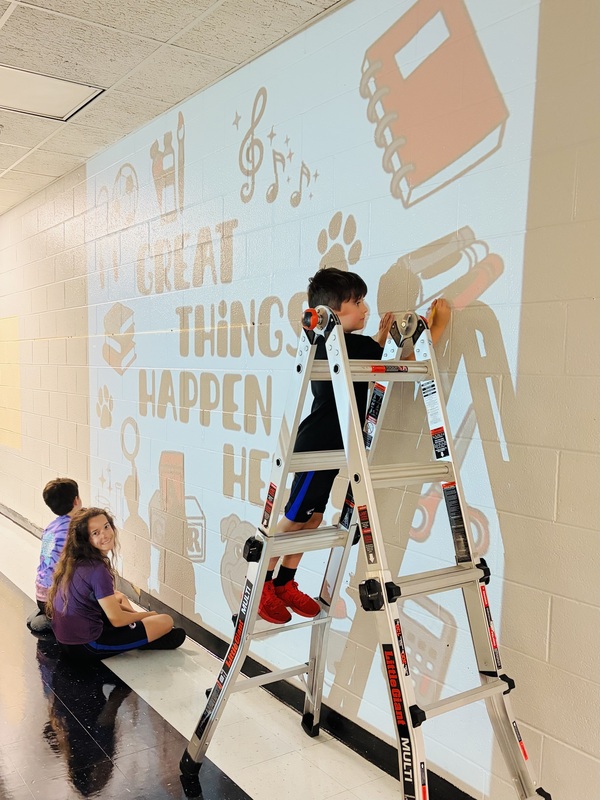 kids helping paint a mural on a wall using a projector