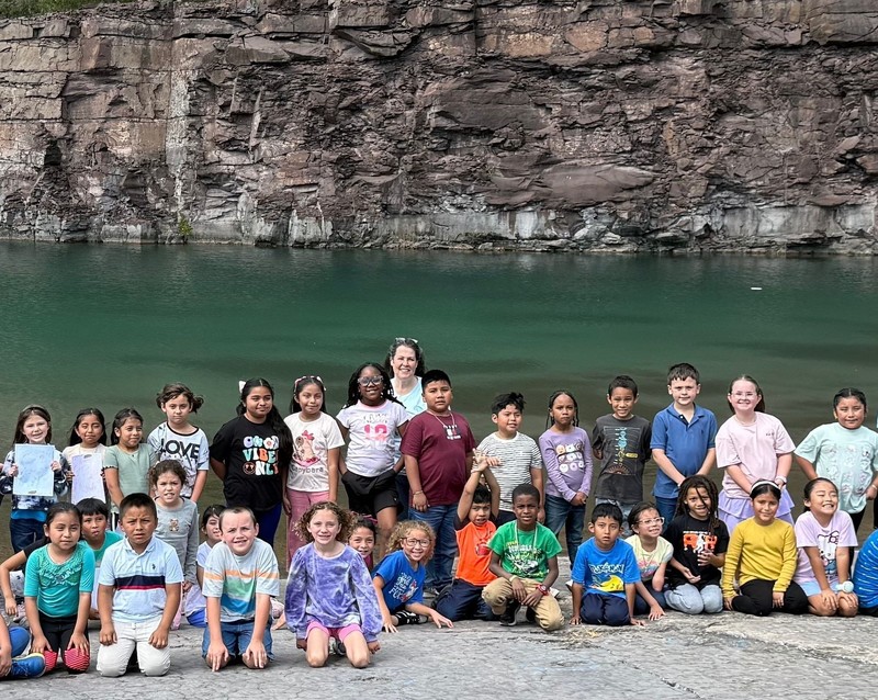group of second grade students posing together at edge of a quarry lake with the rock wall behind them