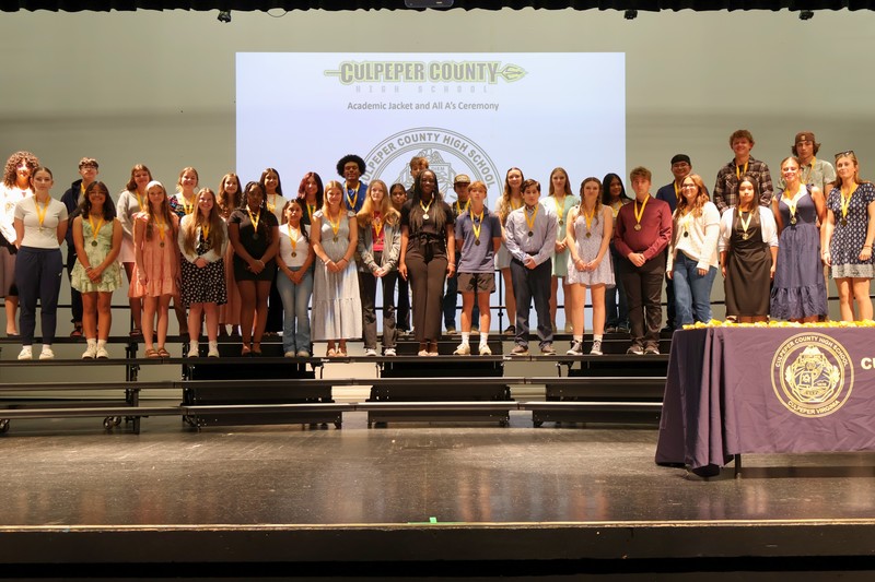 students standing on risers on school stage wearing medals