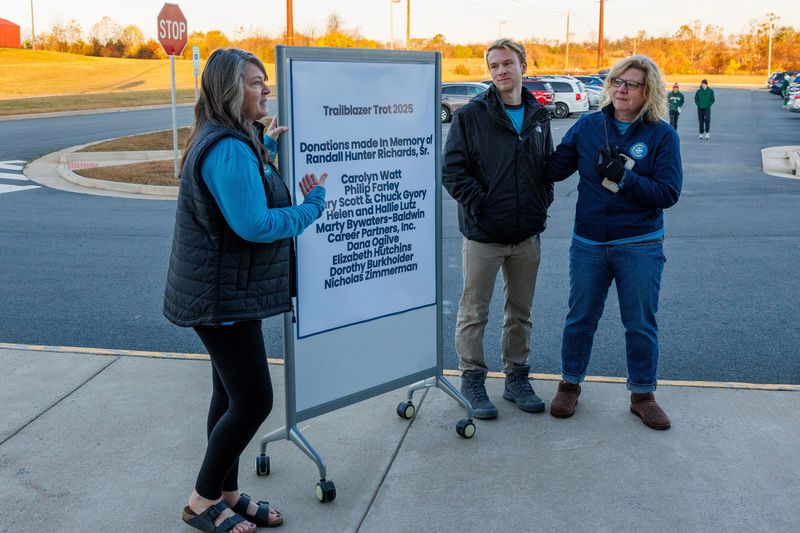 a lady standing next to a board that lists donors for the trailblazer trot with a young man and his mother on the other side