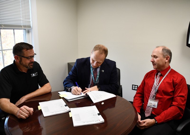 dr brads sitting at table signing a contract with taft rep looking on on the left and ccps employee on the right