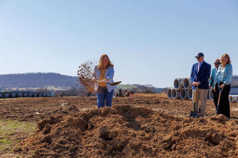 principal angie fiscus shoveling dirt while others look on smiling at the mountain run elementary groundbreaking ceremony