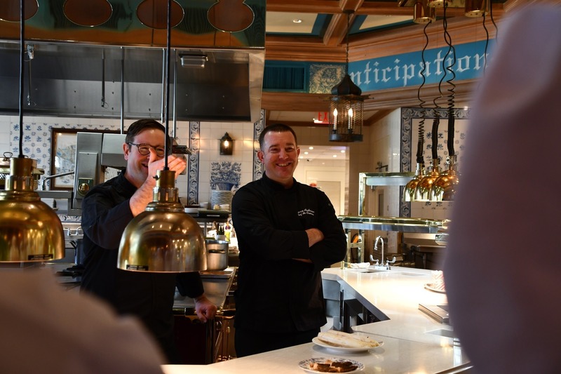 chefs in brigrade style kitchen speaking to students and smiling