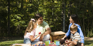 A family is gathered in a park, sitting on a picnic blanket and sharing food.
