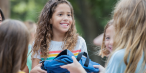 girl with long brown hair and t-shirt  receiving a backpack of supplies from a teacher