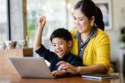 Mother and small son sitting at table working on  a laptop.