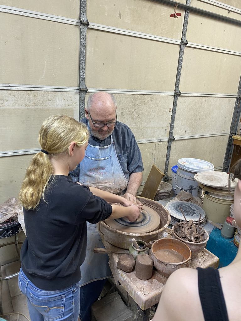 An art student is working with a teacher to throw clay on the wheel.