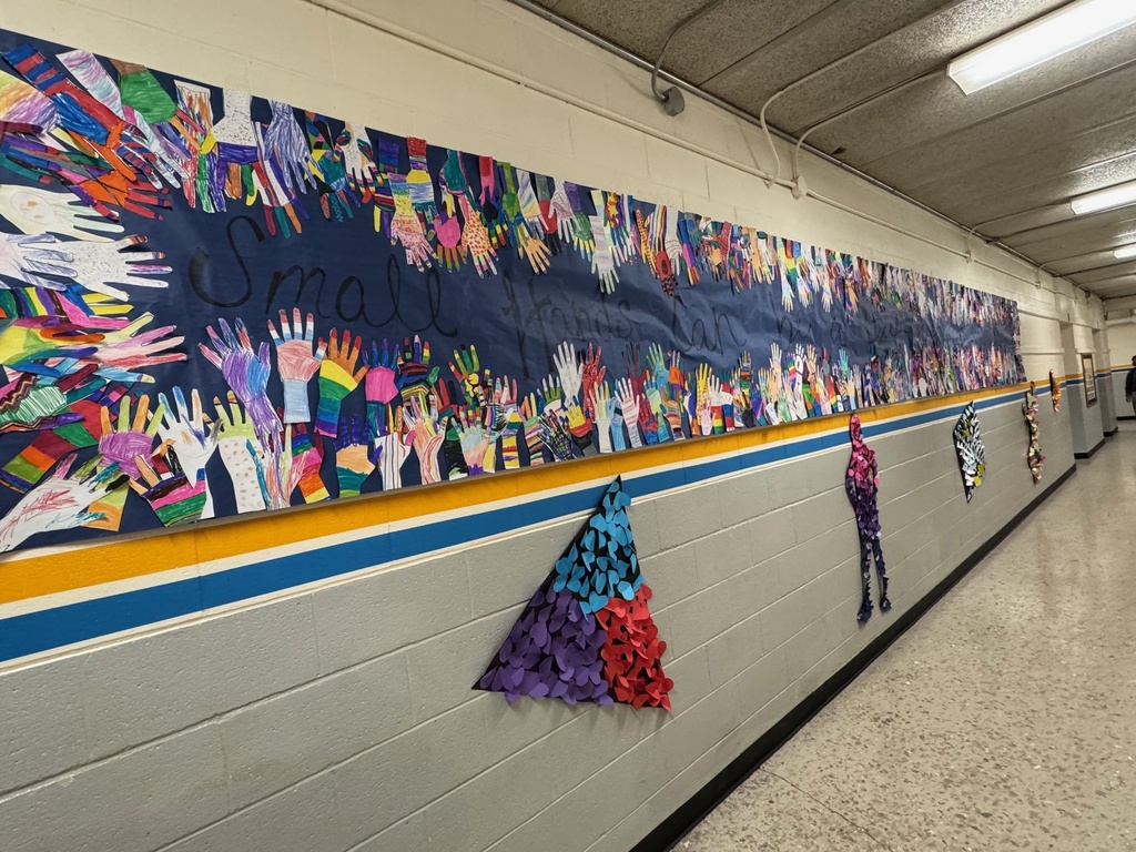 A long hallway mural featuring dozens of handprint cutouts colored with unique patterns, surrounding the phrase "Small Hands Can..." in cursive. Below the mural, several human silhouettes are decorated with layered paper shapes in different colors.