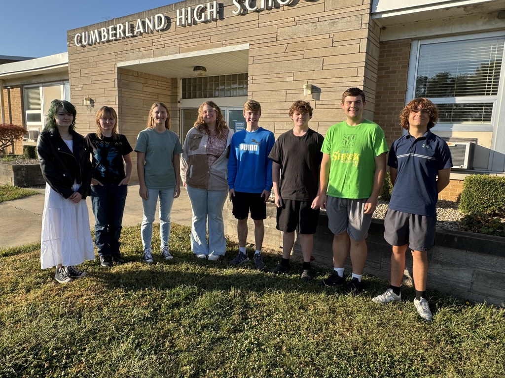Members of the ensemble are standing in front of the high school.