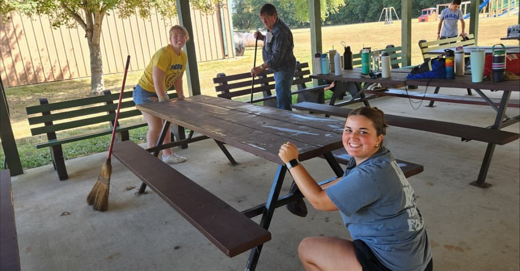 Two students are wiping down a picnic table.