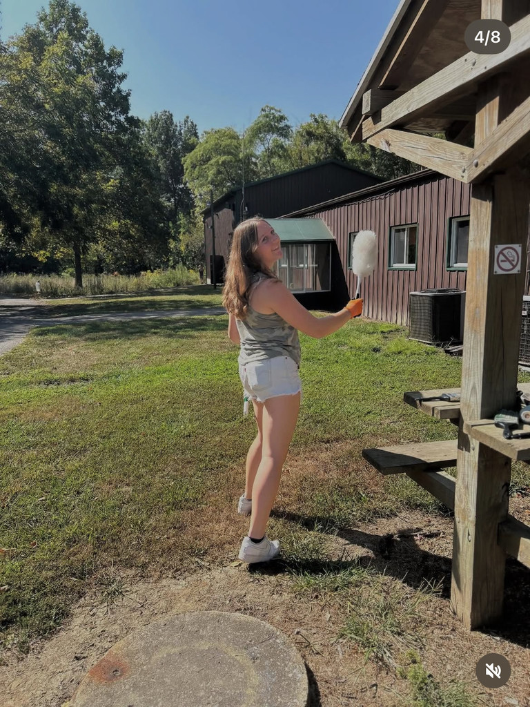 A student is dusting cobwebs off of a picnic area.