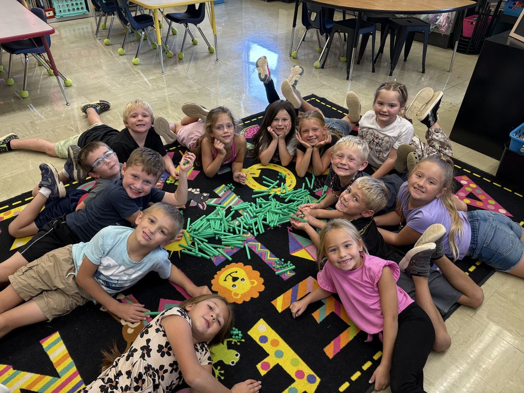 The students are laying in a circle on the carpet with the tens blocks in the middle of the circle.