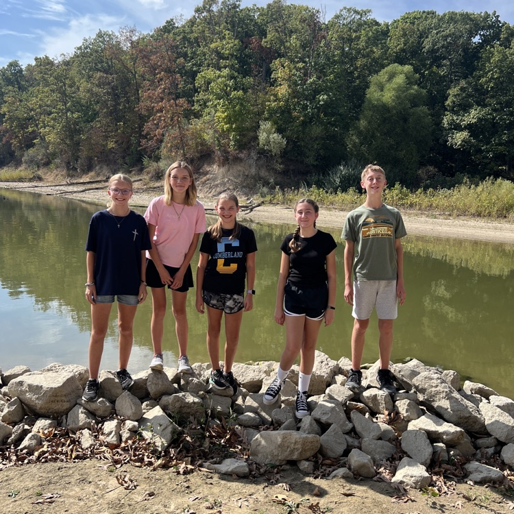 The team is standing together on some rocks near the lake