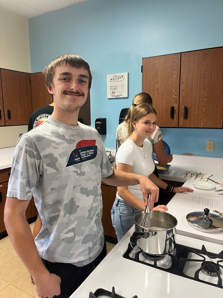 A student is stirring the item in the pot. Another student is looking on.