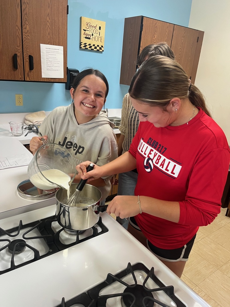 A student is pouring liquids into the pot. The second student is holding the pot and stirring.