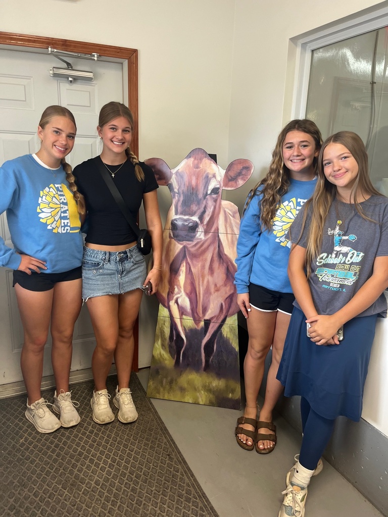 Four students are shanding next to a cow cut out. They are against a white wall.