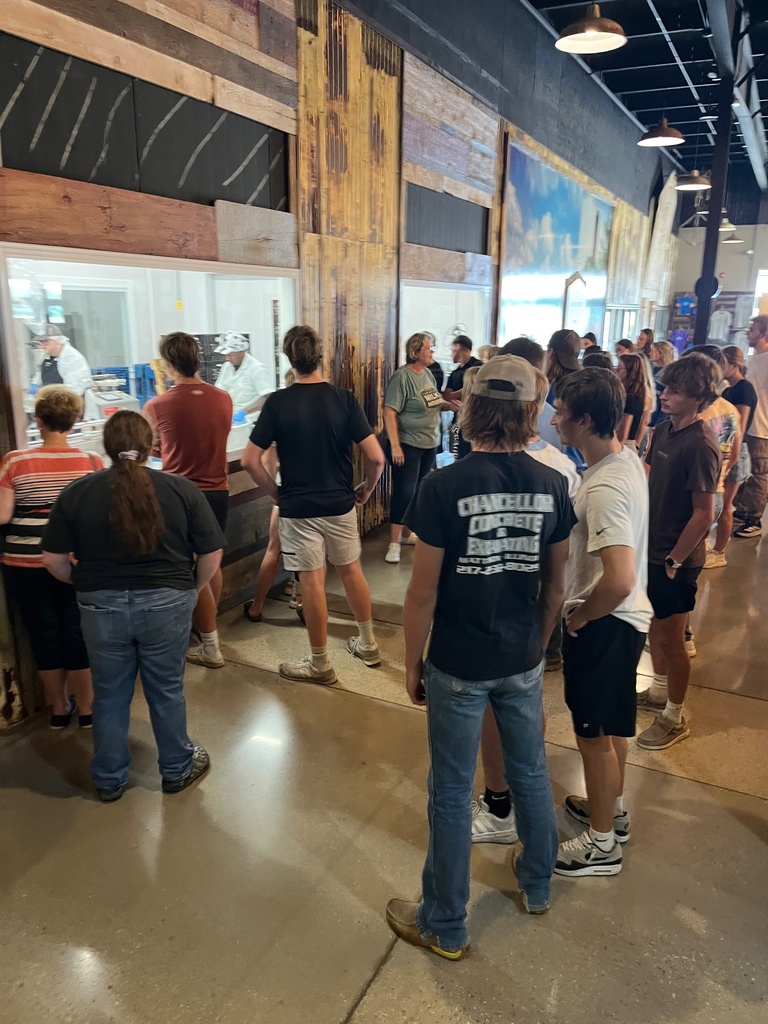 Students are gathered to watch the employees make cheese. They are behind a glass window.