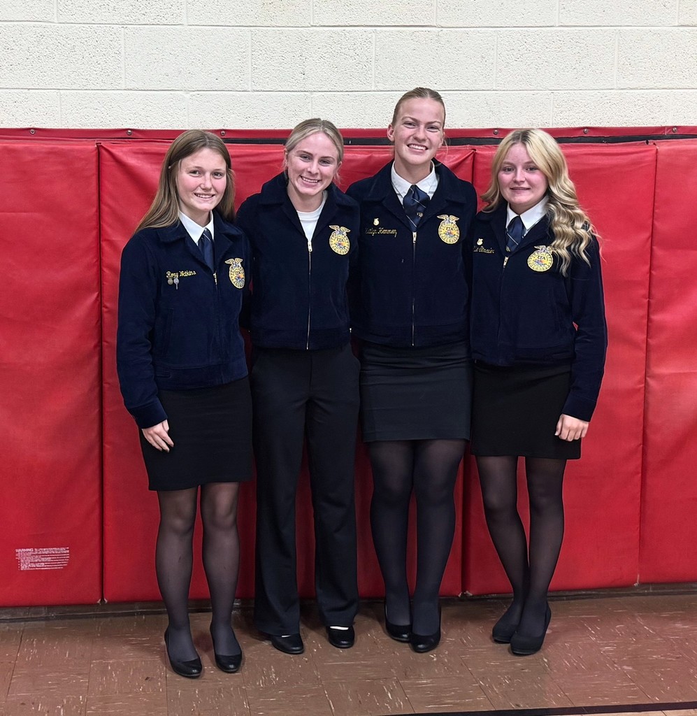 The four students are pictured in front of a red mat. They are wearing their FFA uniforms.