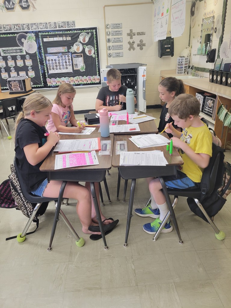 A group of students is sitting together at their desks. They are looking through papers to find clues. They are using highlighters.