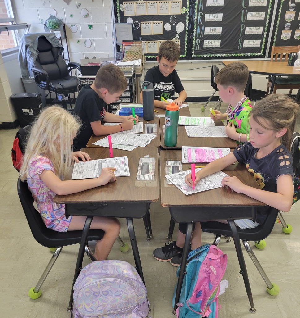 A group of students is sitting together at their desks. They are looking through papers to find clues. They are using highlighters.