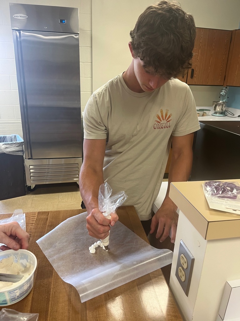 The students is piping icing onto wax paper. They are small white dots.