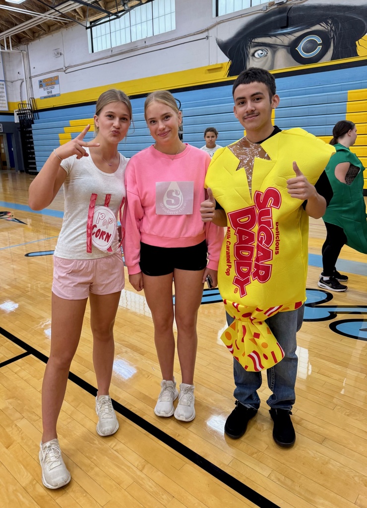Three students are standing together. One is dressed as popcorn. Another is dressed as pink starbursts. While the third is dressed as sugar daddy candy.