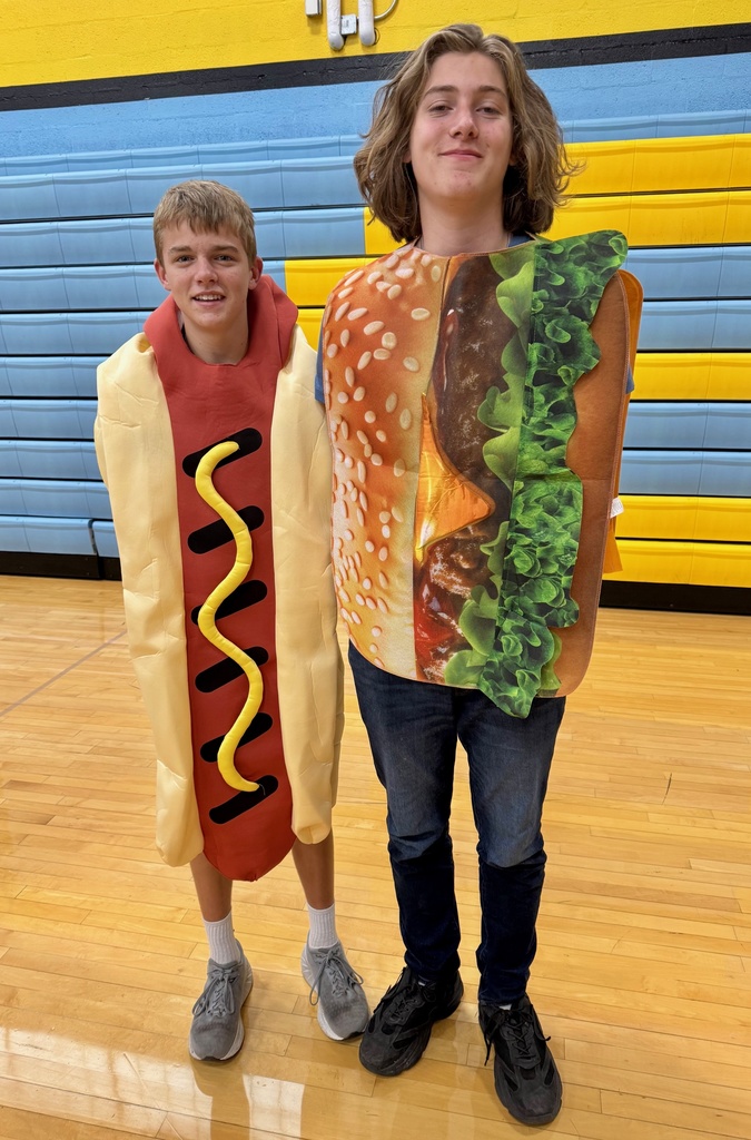Two students are standing side by side. One is wearing a hotdog costume. The second is wearing a cheeseburger costume.