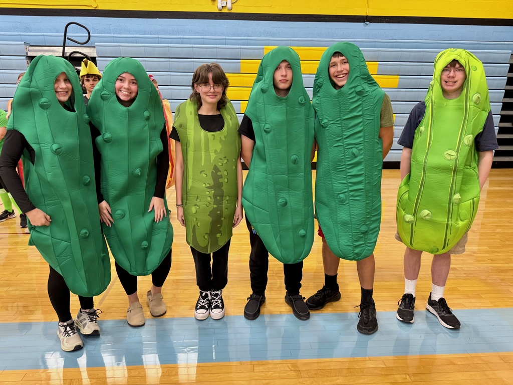 Six student sare standing side by side. They are each wearing pickle costumes.