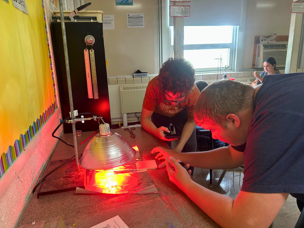 Students are watching the heat lamp. One student is timing to watch the affect of heat over a period of time.