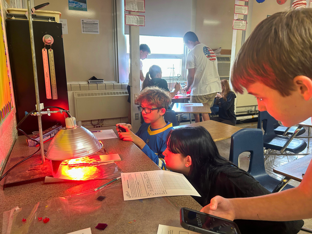 Students are watching the heat lamp. One student is timing to watch the affect of heat over a period of time.