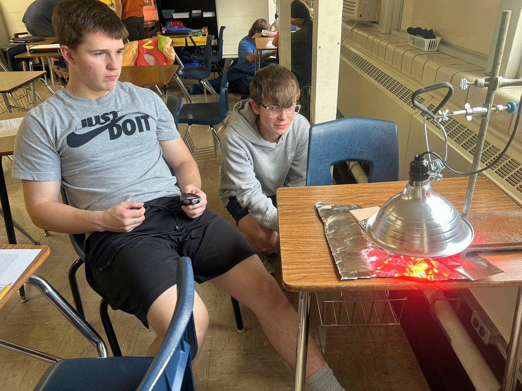 Students are watching the heat lamp. One student is timing to watch the affect of heat over a period of time.