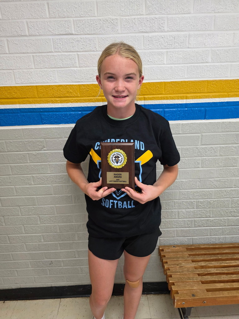 One student is standing against a wall holding her award.
