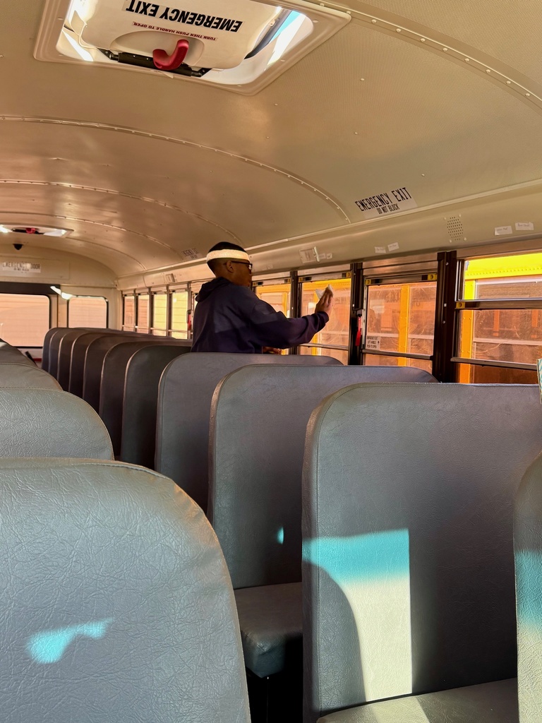 A student is standing between the seats. He is wiping a window with a rag.