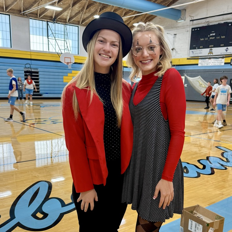 two students are standing side-by-side. They are both wearing red and black. They are dressed up as ringmasters.
