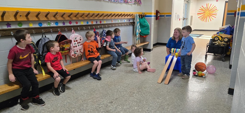 A student rolls a ball down the ramp. The others look on.