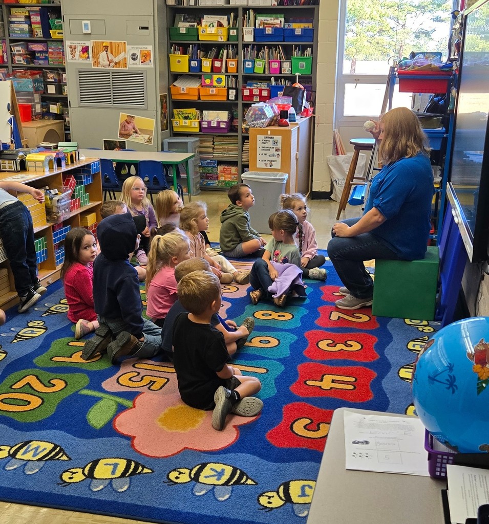 The teacher is holding a ball. The students are looking at the teacher.