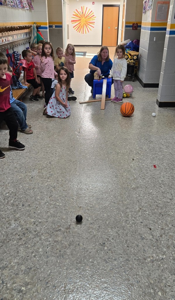 A student rolls a ball down the ramp. The others look on.