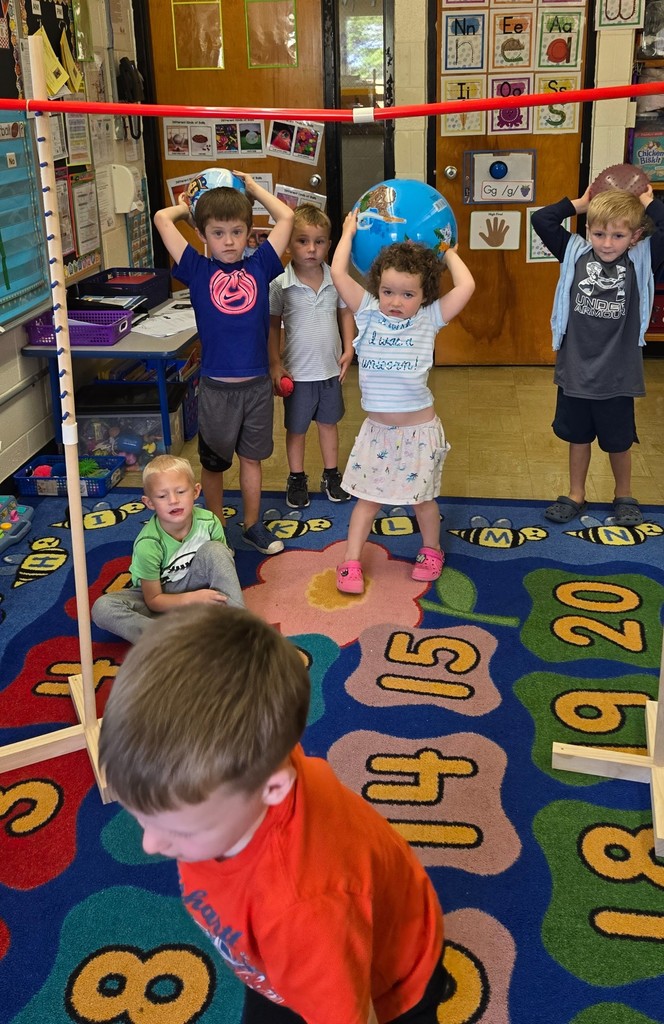 A student is holding a ball over her head. She is attempting to throw it over the bar.