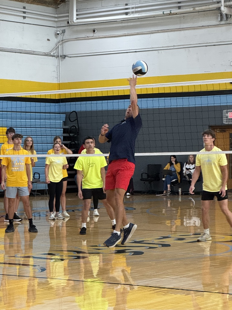 Dr. Thompson is hitting the ball over the net. His arm is raised over his head and his back is to the net.