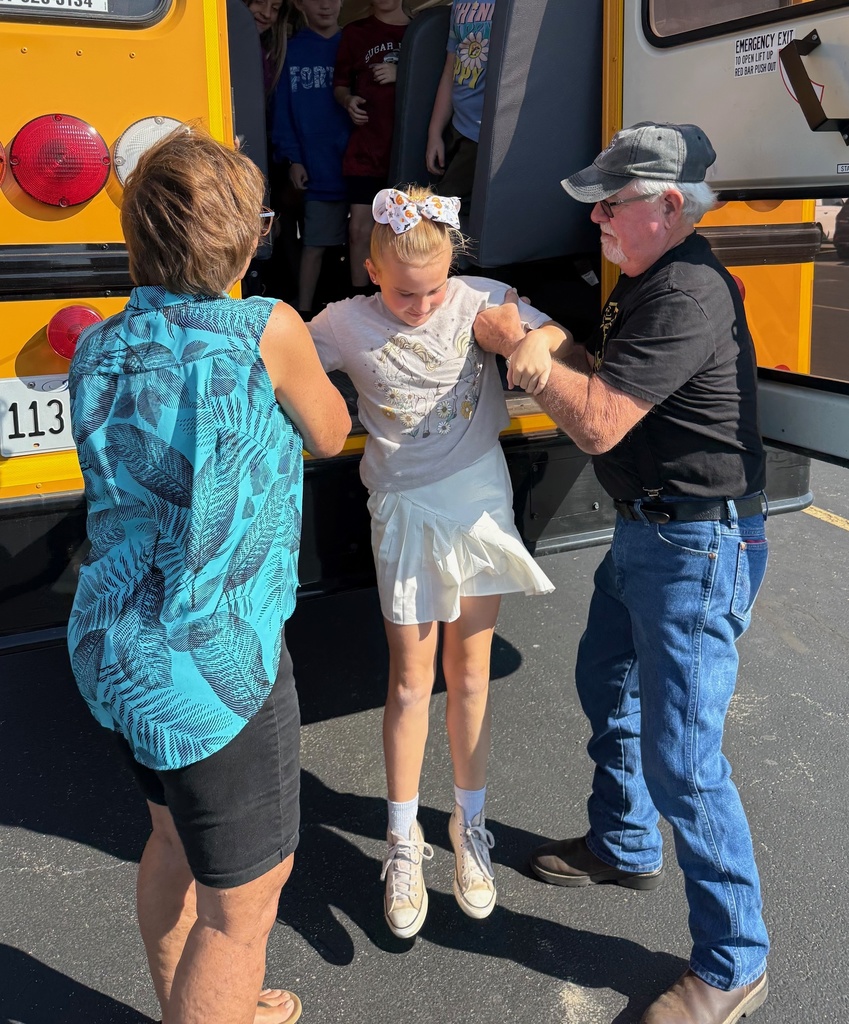 Two adults are helping a student get out of the back door on the bus. The adults are supporting her arms as she jumps.