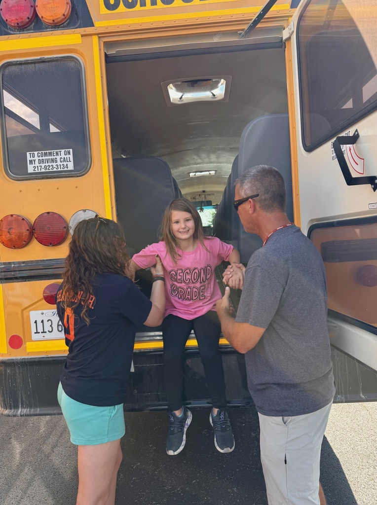 Two adults are helping a student get out of the back door on the bus. The adults are supporting her arms as she jumps.