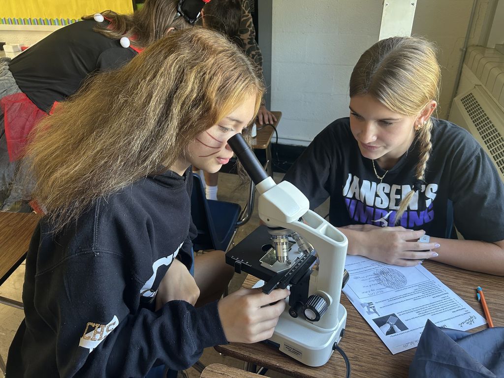 A student is looking through the microscope. Another student is watching.