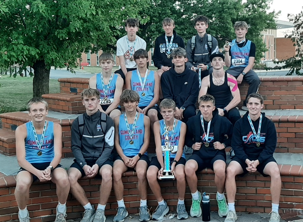 The boys team is sitting on the concete walls. They are wearing their medals and holding their trophy.