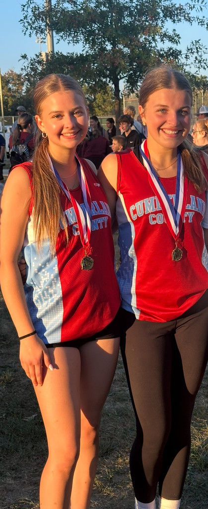 The two all-conference girls runners are standing side by side. They are wearing their medals.
